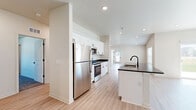 Located in Independence, Missouri, this single-story home offers a thoughtfully designed open-concept floor plan that maximizes comfort and functionality. The kitchen is a standout feature, showcasing crisp white shaker cabinetry, dark granite countertops, stainless steel appliances including a range, microwave, refrigerator, and dishwasher, and a central island with a black matte faucet — all set atop light-toned luxury vinyl plank flooring that flows seamlessly through the main living areas. The living room is bright and airy, with sliding glass doors that open to an outdoor view, allowing natural light to pour in. The spacious primary bedroom features plush carpet, a ceiling fan, and direct access to an en-suite bathroom equipped with a double-sink vanity with granite countertops, white cabinetry, black hardware accents, and a walk-in glass shower. The second bedroom is generously sized with carpet flooring and ample natural light from a large window. A second full bathroom includes a tub-shower combination with black fixture accents. Both bedrooms are complemented by well-organized closets featuring wire shelving systems. The home's neutral palette and modern finishes create a clean, move-in-ready ambiance throughout.