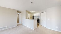 This thoughtfully designed single-floor residence offers a comfortable and functional layout across six distinct spaces. The open-concept living area flows seamlessly into the kitchen, which is separated by a peninsula-style half-wall with an integrated sink. The kitchen is outfitted with stainless steel appliances, including a refrigerator and electric range, white shaker-style cabinetry, a tile backsplash, and light wood-look flooring that adds warmth to the space. Ample cabinet storage makes this kitchen as practical as it is clean in appearance. The carpeted living room benefits from natural light streaming through large windows fitted with white horizontal blinds, creating a bright and inviting atmosphere. A hallway connects the main living areas to the private bedroom, which features plush carpeting, neutral wall tones, natural light from a window, and access to a dedicated closet. The full bathroom is finished with wood-look flooring, a white vanity with drawers and cabinet storage, a framed mirror, and a tiled tub-shower combination with a grab bar. Clean lines and a neutral color palette throughout lend the space a cohesive and modern character.
