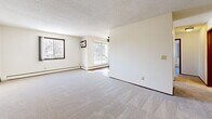 This single-floor residential unit offers a practical and well-organized layout across several rooms. The expansive living area is finished with plush carpeting, textured ceilings, and multiple windows that bring in generous natural light along with views of surrounding trees. A ceiling fan and a sliding glass door leading to a balcony add comfort and accessibility to the space. Baseboard heating units are present throughout, ensuring consistent warmth.

The galley-style kitchen is equipped with rich, dark wood cabinetry, white appliances including a full-size refrigerator and range, a double sink with light-toned countertops, and wood-look flooring. A bathroom is conveniently accessible directly from the kitchen corridor.

The unit includes multiple bedrooms, each carpeted and featuring ceiling fans, natural light from windows with outdoor wooded views, and baseboard heaters. The primary bedroom boasts a full wall of sliding wood-panel closet doors, providing ample storage. Additional bedrooms offer a clean, neutral palette with dark wood trim accents.

The bathroom is tiled, featuring a shower/tub combination, a vanity with mirror cabinet, and wood-look flooring. Throughout the unit, dark wood trim provides a consistent design detail, complementing the light, neutral walls and creating a cohesive, functional living environment.