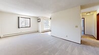This single-floor residential unit offers a practical and well-organized layout across several rooms. The expansive living area is finished with plush carpeting, textured ceilings, and multiple windows that bring in generous natural light along with views of surrounding trees. A ceiling fan and a sliding glass door leading to a balcony add comfort and accessibility to the space. Baseboard heating units are present throughout, ensuring consistent warmth.

The galley-style kitchen is equipped with rich, dark wood cabinetry, white appliances including a full-size refrigerator and range, a double sink with light-toned countertops, and wood-look flooring. A bathroom is conveniently accessible directly from the kitchen corridor.

The unit includes multiple bedrooms, each carpeted and featuring ceiling fans, natural light from windows with outdoor wooded views, and baseboard heaters. The primary bedroom boasts a full wall of sliding wood-panel closet doors, providing ample storage. Additional bedrooms offer a clean, neutral palette with dark wood trim accents.

The bathroom is tiled, featuring a shower/tub combination, a vanity with mirror cabinet, and wood-look flooring. Throughout the unit, dark wood trim provides a consistent design detail, complementing the light, neutral walls and creating a cohesive, functional living environment.