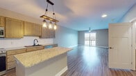 This single-floor residence offers a thoughtfully designed open-concept layout that seamlessly connects the kitchen, dining, and living areas. The kitchen is a standout feature, equipped with warm-toned wood cabinetry, granite countertops, a central island with pendant lighting fashioned from rustic wood and lantern-style fixtures, and a full suite of stainless steel appliances including a refrigerator, range, microwave, and dishwasher. A matte black faucet at the sink adds a contemporary accent. Durable hardwood-style flooring flows throughout the main living areas, complementing the neutral gray walls and crisp white trim.

The living area is generously proportioned, featuring a ceiling fan and a sliding glass door that opens to a balcony, allowing natural light to fill the space. Bedrooms are carpeted for comfort and include ceiling fans and closets, with one bedroom offering direct access to a private bathroom. Bathrooms are finished with granite-topped wood vanities, illuminated mirrors, and hardwood-style flooring. One full bathroom includes a tub-shower combination. A dedicated laundry area houses a full-size Samsung washer and dryer, adding everyday convenience to this well-appointed residence.