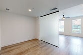 This single-floor unit offers a thoughtfully designed layout with a clean, modern aesthetic throughout. Light wood-tone flooring runs continuously across the main living areas, lending warmth and visual continuity to the space. A standout architectural feature is the frosted glass sliding partition framed in matte black, which divides the living area from the kitchen zone while allowing diffused light to pass through, maintaining an open and airy feel.

The kitchen is outfitted with white cabinetry, stainless steel appliances including a full-size refrigerator and dishwasher, open shelving, and a dark-finished faucet, reflecting a contemporary design sensibility. Recessed lighting provides even illumination throughout, complemented by a ceiling fan visible in the living area. A window allows natural light to enter, adding brightness to the space.

The hallway connects the main living areas to the bathroom, which features large-format light tile flooring, a white vanity with ample cabinetry and black hardware, a wide framed mirror, and a marble-accented shower enclosure. Black grab bars provide additional functionality. The overall palette—white walls, neutral tones, and black accents—creates a cohesive, minimalist atmosphere throughout.