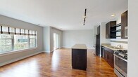 This 2-bedroom, 2-bathroom residence offers a thoughtfully designed single-floor layout that balances comfort and functionality. The open-concept kitchen and living area serves as the heart of the home, featuring rich hardwood-style flooring that runs throughout. The kitchen is outfitted with dark espresso cabinetry, granite countertops, a full suite of stainless steel appliances including a refrigerator, gas range, microwave, and dishwasher, and a central island with additional storage and prep space. Track lighting overhead adds both style and practicality. The living area is bright and airy, benefiting from natural light through large windows and a sliding glass door that opens to a private balcony overlooking a landscaped courtyard and multi-story residential exterior. Both bedrooms are carpeted and generously sized, with the primary bedroom offering notable square footage, built-in closet storage, and a calm, neutral palette. The second bedroom features adjustable shelving built into the closet area. The bathrooms include a tub-shower combination with clean white tile accented by a dark horizontal border. Neutral gray walls throughout create a cohesive, modern aesthetic across the entire residence.