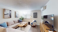 This single-floor residence offers a thoughtfully designed layout with a cohesive modern aesthetic throughout. The living room serves as the heart of the space, featuring warm hardwood-style flooring, a textured ceiling, and a wall-mounted split air conditioning unit for year-round comfort. Natural light filters in through a large window dressed with horizontal blinds, illuminating the neutral-toned walls and complementing the curated furnishings, including a spacious sectional sofa, a live-edge wood coffee table, and a cozy accent chair. Decorative wall art and indoor greenery add character and warmth to the room, while a wooden media console with a flat-screen TV anchors one side of the space.

The kitchen is clean and contemporary, showcasing two-tone cabinetry with white upper cabinets and natural wood lower cabinets, contrasted by bright white countertops. Stainless steel appliances, including a range, over-the-range microwave, and dishwasher, provide a sleek, functional cooking environment.

The bedroom is serene and well-proportioned, with hardwood-style flooring, a textured ceiling, and direct access to a bathroom. A warm wood dresser and soft area rug contribute to the room's comfortable, welcoming atmosphere. Closet access is conveniently located within the bedroom corridor.