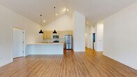 Located at 239 Water Street in West Bend, Wisconsin, this single-floor, 3-bedroom, 2-bathroom home combines modern design with functional living. The open-concept kitchen and living area is the heart of the home, anchored by soaring vaulted ceilings that create a bright, airy atmosphere. The kitchen is well-appointed with light wood shaker-style cabinetry, a subway tile backsplash, stainless steel appliances including a refrigerator and range with microwave, and a large center island with a white countertop and undermount sink, illuminated by striking pendant lights overhead. Warm hardwood-style flooring flows seamlessly throughout the home, complementing the clean white walls and abundant natural light. The primary bedroom is generously sized, featuring vaulted ceilings, a wide sliding closet, and large windows that invite outdoor views and sunlight. The additional bedrooms are well-proportioned with high ceilings and their own closet access. The hallway connects rooms via sliding barn-style doors, adding a sleek, contemporary touch. The bathrooms are finished in a clean, minimal style, with one featuring a walk-in shower with a curved rod and grab bar. The overall ambiance is fresh, modern, and move-in ready.