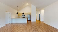 Located at 239 Water Street in West Bend, Wisconsin, this single-floor, 3-bedroom, 2-bathroom home combines modern design with functional living. The open-concept kitchen and living area is the heart of the home, anchored by soaring vaulted ceilings that create a bright, airy atmosphere. The kitchen is well-appointed with light wood shaker-style cabinetry, a subway tile backsplash, stainless steel appliances including a refrigerator and range with microwave, and a large center island with a white countertop and undermount sink, illuminated by striking pendant lights overhead. Warm hardwood-style flooring flows seamlessly throughout the home, complementing the clean white walls and abundant natural light. The primary bedroom is generously sized, featuring vaulted ceilings, a wide sliding closet, and large windows that invite outdoor views and sunlight. The additional bedrooms are well-proportioned with high ceilings and their own closet access. The hallway connects rooms via sliding barn-style doors, adding a sleek, contemporary touch. The bathrooms are finished in a clean, minimal style, with one featuring a walk-in shower with a curved rod and grab bar. The overall ambiance is fresh, modern, and move-in ready.