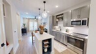 Located at 120 Whitby Lane in Birmingham, Alabama, this efficiently designed one-bedroom, one-bathroom residence offers a thoughtfully organized single-floor layout. The open-concept kitchen and living area serves as the heart of the home, where a striking two-tone kitchen island with navy blue lower cabinets and a crisp white quartz countertop takes center stage, illuminated by elegant glass pendant lights. The kitchen features white shaker cabinetry with matte black hardware, a classic subway tile backsplash, stainless steel appliances, open shelving, and durable hardwood-style flooring. The adjacent living room is bright and welcoming, with large windows and a glass-paned door that frame outdoor views and flood the space with natural light. A ceiling fan adds comfort overhead. The bedroom offers a serene retreat with multiple windows, a ceiling fan, plush carpeting, and access to two closets, including a walk-in closet with wire shelving. The bathroom is finished with marble-style tile surrounding the soaking tub and shower, matte black fixtures, and a clean vanity. The overall aesthetic is modern and cohesive, balancing contemporary finishes with warm, inviting touches throughout.