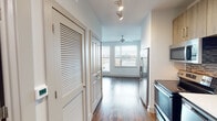 Located along Sixth Avenue South in Birmingham, Alabama, this single-floor unit offers a thoughtfully designed interior with a clean, contemporary aesthetic throughout. Rich wood-look flooring extends across the living areas, complementing the neutral white walls and creating a warm yet modern atmosphere.

The kitchen is efficiently appointed, featuring warm-toned wood cabinetry with sleek bar-pull hardware, a mosaic tile backsplash, white quartz countertops, and a full suite of stainless steel appliances including a French door refrigerator, electric range, built-in microwave, and dishwasher. Track lighting and louvered storage doors are positioned along the hallway leading into the main living area.

The open living space is bright and airy, with a bank of large windows fitted with blinds that frame elevated views of the surrounding Birmingham streetscape. A ceiling fan provides additional comfort overhead.

The bathroom is well-finished, with a wood-toned vanity, white countertop, a glass-enclosed walk-in tiled shower with a built-in bench, and open built-in shelving for storage. Wood-look tile flooring ties the bathroom's design to the rest of the unit cohesively.