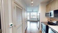 Located along Sixth Avenue South in Birmingham, Alabama, this single-floor unit offers a thoughtfully designed interior with a clean, contemporary aesthetic throughout. Rich wood-look flooring extends across the living areas, complementing the neutral white walls and creating a warm yet modern atmosphere.

The kitchen is efficiently appointed, featuring warm-toned wood cabinetry with sleek bar-pull hardware, a mosaic tile backsplash, white quartz countertops, and a full suite of stainless steel appliances including a French door refrigerator, electric range, built-in microwave, and dishwasher. Track lighting and louvered storage doors are positioned along the hallway leading into the main living area.

The open living space is bright and airy, with a bank of large windows fitted with blinds that frame elevated views of the surrounding Birmingham streetscape. A ceiling fan provides additional comfort overhead.

The bathroom is well-finished, with a wood-toned vanity, white countertop, a glass-enclosed walk-in tiled shower with a built-in bench, and open built-in shelving for storage. Wood-look tile flooring ties the bathroom's design to the rest of the unit cohesively.