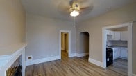 This single-floor residence combines classic architectural charm with a clean, neutral aesthetic. The main living area showcases warm hardwood-style flooring that runs throughout, complemented by crisp white baseboards that frame each room with a polished finish. A ceiling fan with a light fixture is centrally mounted, providing both ventilation and ambient lighting to the space.

A standout architectural detail is the elegant arched alcove built into the wall, adding a timeless character to the interior and offering a decorative niche that breaks up the clean lines of the room. A traditional rectangular doorway with white trim leads into a hallway, connecting the living area to additional rooms beyond. The hallway, visible through the doorway, continues the same warm flooring, suggesting a cohesive design throughout the home.

The walls are finished in a soft, warm greige tone that pairs naturally with the flooring, creating a calming and inviting ambiance. The open and uncluttered layout of the main room allows for flexible furnishing arrangements. Overall, the space reflects a well-maintained interior with thoughtful architectural touches that blend traditional design elements with a simple, functional layout suited for comfortable everyday living.