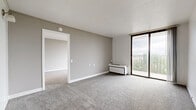 Located at 4032 N Main St in Dayton, Ohio, this one-bedroom, one-bathroom unit offers a practical and comfortable layout across a single floor. The living room is generously proportioned, featuring soft gray carpeting, neutral-toned walls, and a full-width sliding glass door that opens to a private balcony. The balcony provides open outdoor views of the surrounding Dayton skyline and greenery, filling the living area with abundant natural light. The bedroom is a well-sized private retreat, also carpeted, with its own sliding glass door access and views to the outdoors. A hallway connects the main living spaces and provides organizational flow throughout the unit. The galley-style kitchen is efficiently designed, featuring warm honey-toned wood cabinetry, white appliances including a range and refrigerator, light countertops, and durable hardwood-style flooring that adds a welcoming contrast to the cabinetry. The full bathroom is clean and straightforward, equipped with a tub and shower combination, a grab bar for added accessibility, and hardwood-style flooring. Throughout the unit, the design maintains a simple, neutral palette that offers a bright and move-in-ready atmosphere suitable for comfortable everyday living.