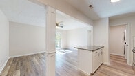 This well-appointed 3-bedroom, 1-bathroom residence in Loveland, Ohio offers an efficient and thoughtfully designed single-floor layout. The open-concept living and kitchen area serves as the heart of the home, featuring light hardwood-style flooring, a ceiling fan with light fixture, and a textured ceiling. The kitchen is outfitted with white shaker cabinetry, a classic subway tile backsplash, granite-patterned countertops, stainless steel appliances including a refrigerator, microwave, and range, and a peninsula with additional cabinet storage — all framed by a decorative white column that defines the transition to the living space. Sliding glass doors in the living area open to a private balcony with lush tree views, flooding the room with natural light. The three bedrooms include a spacious primary bedroom with its own ceiling fan and direct balcony access, while the secondary bedrooms feature soft carpet, ceiling fans, and windows overlooking mature greenery. Four closets throughout the unit provide generous storage. The full bathroom includes a tiled tub-shower combination with brushed nickel fixtures. A dedicated laundry area and a connecting hallway round out this practical and comfortable home.