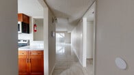 This single-floor, one-bedroom, one-bathroom unit offers a practical and efficient layout across a comfortable footprint. Polished marble-look ceramic tile flows consistently throughout the entire space, lending a clean and elegant aesthetic to every room.

The central hallway connects all areas of the unit, lined with textured walls and a wall sconce light fixture. To one side, the kitchen features warm cherry wood cabinetry and granite countertops, providing a functional workspace. The open living room is spacious, bathed in natural light from a full sliding glass door that leads to a private balcony with outdoor views, creating an airy and inviting atmosphere.

The bedroom is a well-sized, tranquil retreat with a ceiling fan, a window fitted with horizontal blinds for light control and privacy, and direct access to the hallway. The bathroom is appointed with a rich cherry wood vanity topped with granite countertops, a framed mirror, and a clean, neutral color palette.

Throughout the unit, textured popcorn ceilings, neutral warm-toned walls, and clean white baseboards maintain a cohesive and understated design. The space is efficiently organized, making it an informative example of a compact yet complete single-bedroom residential layout.