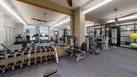 Located at 2250 Hawkins St. in Charlotte's South End neighborhood, this fitness center is a well-appointed, single-floor facility designed to support a comprehensive workout experience. The space is organized into distinct functional zones, allowing users to seamlessly transition between cardio, strength training, and functional fitness activities.

The cardio section features a row of True treadmills and elliptical machines, each equipped with individual displays, positioned along one wall beneath bright linear overhead lighting and ceiling fans that promote air circulation throughout the space. Adjacent to the cardio area, a robust selection of Precor and Cybex strength machines provides targeted muscle training options, complemented by a full rack of dumbbells for free weight exercises.

Large framed mirrors line key sections of the walls, amplifying the sense of openness and allowing users to monitor their form. Exposed concrete columns add an industrial architectural character, while the durable rubber flooring throughout ensures both safety and comfort underfoot.

A dedicated functional training zone, enclosed by sleek black-framed glass partition doors with decorative frosted patterning, houses stability balls, medicine balls, resistance bands, a cable machine, and plyometric boxes — offering a versatile space for dynamic and group-style workouts. Natural light filters in through windows, contributing to an energizing and welcoming atmosphere.