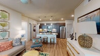 Located on Cimarron Boulevard in Corpus Christi, Texas, this single-story residence offers a well-designed open-concept floor plan that seamlessly connects the main living areas. Light wood-tone flooring runs throughout the common spaces, contributing to a bright and cohesive feel.

The kitchen serves as a central focal point, outfitted with dark espresso cabinetry, a subway tile backsplash, stainless steel appliances, and a granite-topped island with bar seating and pendant lighting overhead. Adjacent to the kitchen, a dedicated dining area includes a built-in desk nook with dark shelving, offering a functional workspace. The living room benefits from natural light through large windows and a glass door leading to an outdoor area, with a ceiling fan providing additional comfort.

The bedrooms feature plush carpeting, ceiling fans, and generous window treatments that invite natural light. Both bathrooms are finished with wood-look flooring, dark vanity cabinetry, granite countertops, and tub-shower combinations.

Throughout the residence, crown molding, recessed lighting, and consistent neutral tones create a polished, cohesive atmosphere with a subtle coastal character.