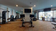 This fitness center at 1145 Chambers Rd in Columbus, Ohio, offers a comprehensive and well-appointed exercise facility designed to support a full range of workout routines. The single-level space is finished with durable textured carpeting throughout and benefits from recessed lighting that keeps the environment bright and functional.

The cardio section is prominently featured, housing a row of True-brand treadmills and elliptical machines, each equipped with individual screens for entertainment or workout tracking. Alongside these, dual stationary cycling bikes with digital displays provide dedicated options for low-impact training. A wall-mounted flat-screen television is positioned above the cycling area for shared viewing.

The strength training section features a selection of cable machines, a multi-function weight station, a leg press, and an adjustable bench, catering to both beginner and advanced users. A dedicated free weights area includes a rack stocked with medicine balls and kettlebells of varying sizes.

Full-length mirrors line multiple walls, visually expanding the space and allowing users to monitor their form. Large sliding glass doors on one side of the room flood the area with natural light and offer direct views of an outdoor courtyard. A ceiling fan overhead adds to the air circulation, and a small service station with storage cabinetry is available within the space.