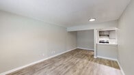 This single-story unit presents a clean, neutral aesthetic throughout, with light-toned walls and wood-look plank flooring running through the main living areas and wet spaces. The open living area is generously proportioned, offering a bright and airy atmosphere enhanced by a large sliding glass door that frames views of an outdoor patio and pool area beyond. A wide window in one room allows additional natural light to fill the space.

The galley-style kitchen is efficiently designed, featuring gray cabinetry, white countertops, a subway tile backsplash, a double stainless steel sink, and stainless steel appliances including a refrigerator and dishwasher. Track lighting illuminates the workspace effectively.

The bedroom is finished with plush carpeting and includes a ceiling fan with light fixture, providing comfort and air circulation. A dedicated laundry area is equipped with washer and dryer hookups, a dryer vent, and a utility shelf above.

The bathroom features wood-look flooring, a soaking tub with tile surround, and a vanity with storage. A central HVAC system serves the unit. Overall, the space maintains a consistent, updated feel throughout.