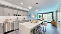 Located at 300 K St in Washington, DC, this thoughtfully designed two-bedroom, one-bathroom residence offers a modern aesthetic with high-quality finishes throughout. The open-concept kitchen and living area serves as the heart of the home, anchored by a striking marble-topped island with seating — ideal for casual dining or entertaining. The kitchen features gray shaker-style cabinetry, stainless steel appliances, white quartz countertops, a subway tile backsplash, and globe pendant lighting that adds a warm, contemporary touch. Wide-plank hardwood flooring runs seamlessly through the main living areas. The living room is bathed in natural light courtesy of floor-to-ceiling sliding glass doors that frame city views and provide direct outdoor access. Both bedrooms continue the floor-to-ceiling window theme, offering urban views and an airy atmosphere. The primary bedroom comfortably accommodates a full sleeping and workspace setup. The bathroom is a standout, featuring a wood-toned vanity with a white countertop, large-format white tile flooring, and a glass-enclosed walk-in shower with bold chevron-patterned gray tile. A clean, well-lit hallway connects the private quarters, completing this polished and functional Washington, DC residence.