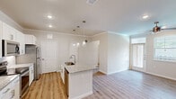 This thoughtfully designed 1-bedroom, 1-bathroom residence offers a comfortable and modern living experience across a single floor. The open-concept kitchen and living area serves as the heart of the home, showcasing light wood-tone luxury vinyl plank flooring, crown molding, and a ceiling fan with recessed lighting. The kitchen is outfitted with crisp white cabinetry, a subway tile backsplash, stainless steel appliances including a refrigerator, range, and microwave, and a granite-topped center island with a built-in sink and elegant pendant lighting overhead. The living area flows naturally from the kitchen, offering an airy, open feel with access to an outdoor balcony overlooking a beautifully landscaped courtyard and sparkling resort-style pool. The bedroom features plush carpeting, a ceiling fan, and dual windows that invite natural light and neighborhood views. The full bathroom includes a subway-tiled soaking tub and shower combination with brushed gold fixtures, granite countertops, and direct access to a generously sized walk-in closet equipped with multi-tier wire shelving throughout. A hallway connects all spaces efficiently, completing this well-organized and stylish residence.