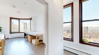 Located at 97 Columbia Heights in Brooklyn Heights, this two-bedroom, two-bathroom residence delivers an efficient and well-organized single-floor layout. The space is defined by its clean, white walls, light wood-style flooring, and an abundance of natural light streaming through large windows that frame breathtaking views of the Manhattan skyline and East River.

The primary bedroom is generously proportioned and features a distinctive curved bay window, maximizing the panoramic cityscape views. Both bedrooms include built-in storage beneath the bed frames, keeping the rooms functional and uncluttered, with a dedicated study area for work or study. The second bedroom also benefits from wide windows with striking views of lower Manhattan.

The kitchen is well-appointed with granite countertops, gray shaker-style cabinetry, a subway tile backsplash, a stainless steel sink, and a full range, offering a polished and practical cooking space. The two bathrooms are finished with classic white subway tile, curtained shower stalls, and built-in mirror cabinetry. One bathroom features a modern vanity with a marble-style countertop and dark wood cabinetry. Three hallways connect the rooms efficiently throughout the unit. The overall ambiance is clean, minimal, and bright, with the iconic Brooklyn Heights location adding exceptional character.