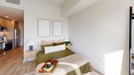 Located at 55 NW 29th St in Miami's vibrant Wynwood neighborhood, this thoughtfully designed unit offers a efficient single-floor layout comprising a living room, kitchen, bathroom, closet, laundry, and utility room. The galley-style kitchen is outfitted with light wood cabinetry extending to the ceiling, white quartz countertops, a subway tile backsplash, and a full suite of stainless steel appliances including a refrigerator with water dispenser, electric range, over-the-range microwave, and dishwasher. Light wood-tone flooring runs throughout the main living areas, lending warmth and visual continuity. The living area is bright and airy, with a window drawing in natural light and offering views of the surrounding cityscape. The bathroom features a clean, modern aesthetic with a wood-framed floating vanity, an integrated white sink, a backlit mirror, large-format neutral floor tiles accented by a geometric patterned inset, and a glass-enclosed shower. The bedroom is serene and simply appointed, with white walls and light flooring creating a calm retreat. A dedicated closet with louvered doors and an in-unit laundry area add practical convenience. The overall design aesthetic is clean and contemporary, emphasizing light tones, minimalist finishes, and efficient use of space throughout.
