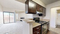 This 590-square-foot, one-bedroom, one-bathroom condo at 1211 S Quebec Way in Denver features vaulted ceilings that create an open, airy atmosphere in the living room, which is anchored by a granite-surround wood-burning fireplace and a sliding glass door leading to a private balcony. High clerestory windows allow natural light to fill the space. The kitchen includes dark wood cabinetry, granite-style countertops, hardwood-style flooring, and stainless steel appliances including a dishwasher. The 130-square-foot bedroom offers carpet flooring, a window with natural light, and direct closet access. The bathroom features wood-style flooring, a tub/shower combination with tile surround, and a dark vanity with granite-style countertop. Baseboard heating is present throughout.
