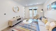 Located at 500 W Broad St in Columbus, Ohio, this single-floor residence offers a thoughtfully designed layout with a clean, modern aesthetic throughout. The open-concept kitchen is a standout feature, showcasing rich dark wood cabinetry, light quartz countertops, a classic white subway tile backsplash, stainless steel appliances, and a large center island with seating — all illuminated by striking black pendant lights and recessed lighting. Light wood-tone flooring flows seamlessly from the kitchen into the living area, where French doors invite natural light and offer views of the surrounding community. The living space is bright and welcoming, with white walls and recessed lighting creating a clean, airy atmosphere. Two well-appointed bedrooms feature plush carpeting, recessed lighting, and windows that bring in natural light and neighborhood views. Each bedroom benefits from direct access to a bathroom. The bathrooms are finished with large-format neutral tile flooring, glass-enclosed showers, dark wood vanities, and matte black hardware accents that complement the modern design language found throughout the residence. The overall ambiance is contemporary and cohesive, with a neutral palette, quality finishes, and functional spaces designed for comfortable urban living in the heart of Columbus.