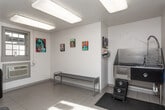Located at 282 N Colonial Homes Cir NW in Atlanta, Georgia, this single-floor Paw Spa is a purpose-built pet grooming facility designed to provide a functional and welcoming environment for pets and their owners. The interior features light tile flooring throughout, white-painted concrete block walls, and bright overhead lighting that keeps the space clean and well-lit.

The main grooming area is equipped with a professional-grade, height-adjustable grooming table, ideal for handling pets of various sizes. A wall-mounted pet dryer provides convenient post-bath drying, while vibrant, colorful dog-themed artwork displayed throughout adds a cheerful and pet-friendly atmosphere. A dedicated bathing station features a deep stainless steel tub with paw print accents and built-in steps, making it easy for pets to access. Anti-fatigue rubber matting surrounds the tub for safety and comfort.

A waiting area offers a bench seat beneath a large window with natural light and additional colorful dog portrait artwork on the walls. The space is climate-controlled with a wall-mounted unit, ensuring year-round comfort. A glass-paneled exterior door provides direct outdoor access and natural light. Clearly posted "Paw Spa Rules" ensure a safe, orderly experience, requiring pets to be leashed, vaccinated, and flea-free at all times.