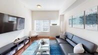 This single-floor residence offers a thoughtfully designed layout that balances comfort and functionality. The kitchen is a standout feature, showcasing rich warm-toned wood cabinetry lining both walls, granite countertops with subtle blue-grey veining, black appliances, and hardwood flooring — creating an efficient galley-style workspace ideal for cooking and entertaining.

The living area is bright and welcoming, with large windows inviting natural light and hardwood floors extending throughout. The space accommodates a comfortable seating arrangement, with clean white walls providing a neutral backdrop that complements contemporary décor.

The bedroom is carpeted and serene, featuring a window that provides additional natural light and an outlook to the outdoors. A notable convenience is the in-unit stacked washer and dryer, accessible directly from the bedroom. A dedicated workspace includes hardwood floors, a clean white desk, and wall-mounted organizational storage.

The bathroom features granite countertops matching the kitchen's aesthetic, warm wood vanity cabinetry, tile flooring, a large mirror, and a shower-tub combination with a decorative curtain. Throughout, the residence maintains a cohesive, neutral color palette that creates a calm and modern ambiance.