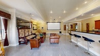 Located at 4401 E 46th St in North Little Rock, Arkansas, this single-floor event and gathering space offers a generously sized, open-concept layout designed for both entertainment and hospitality. The interior is defined by polished granite tile flooring that spans the entire space, crown molding throughout, and recessed lighting complemented by a warm, neutral color palette that creates an inviting ambiance.

The main hall serves as the centerpiece, featuring a large retractable projection screen with a ceiling-mounted projector, making it well-suited for presentations, screenings, or events. Seating areas are appointed with a mix of ornate carved wood furniture, tufted leather Chesterfield sofas, and gilded classical chairs, lending the space a rich, eclectic elegance. Decorative marble columns, framed wall art, and draped windows with rich burgundy valances and blinds add to the refined aesthetic.

A full kitchen anchors one side of the space, outfitted with warm-toned wood cabinetry, dark granite countertops, stainless steel appliances including a range and refrigerator, and a built-in wine rack. A wraparound bar counter with sleek black bar stools provides additional seating and a natural gathering point. Natural light filters in through multiple windows, enhancing the overall warmth and functionality of this versatile space.
