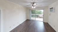 This single-floor residence offers a thoughtfully arranged layout encompassing a living area, kitchen, two bedrooms, and a full bathroom. The living room is finished with dark hardwood-style flooring and crown molding, and is brightened by a sliding glass door that opens onto a private balcony overlooking lush greenery—an inviting feature that brings natural light and outdoor views into the space. A ceiling fan with integrated lighting adds comfort and practicality.

The kitchen is equipped with white cabinetry, dark granite-style countertops, a gas range, over-the-range microwave, and a white refrigerator. The dark wood flooring continues seamlessly from the living area into the kitchen, creating a cohesive aesthetic.

Both bedrooms feature neutral carpeting, crown molding, and ceiling fans with lighting. One bedroom includes a wall-mounted air conditioning unit, while the other offers built-in closet storage with louvered doors. Windows fitted with vertical blinds provide natural light in each room.

The bathroom is finished with light tile flooring and includes a combined tub and shower enclosed by sliding glass doors, a toilet, and a dark-toned vanity countertop, providing a clean and functional design.