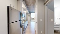 Located in the heart of downtown Grand Rapids, Michigan, this efficiently designed studio unit at 15 Ottawa Ave NW offers a thoughtful layout across a single floor. The combined kitchen and living area is anchored by a sleek galley-style kitchen outfitted with white shaker cabinetry, dark countertops, a tiled backsplash, and a full suite of stainless steel appliances including a refrigerator, microwave, and dishwasher. An in-unit washer is also integrated into the kitchen space, adding everyday convenience. The exposed concrete ceiling throughout lends an industrial character that contrasts elegantly with the light wood-tone flooring and crisp white walls. The living area is bathed in natural light courtesy of expansive floor-to-ceiling windows that frame impressive panoramic views of the Grand Rapids skyline — a defining feature of the space. A barn-style sliding door connects to the bathroom, which includes a tub-shower combination with tiled surround, wood-look flooring, and clean, neutral finishes. The unit's open, minimalist aesthetic and urban location make it a highly functional space with a modern, contemporary ambiance.