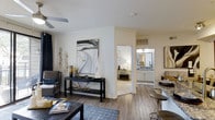 This single-story 1-bedroom, 1-bathroom residence features an open-concept layout that maximizes its well-utilized footprint. The main living area is anchored by wood-look plank flooring that extends throughout, creating a cohesive and warm aesthetic. Crown molding adds a refined architectural detail, while a ceiling fan provides both function and style overhead. The living space flows seamlessly toward the dining area, which is appointed with bar-height seating and dark cabinetry, ideal for casual dining or entertaining. A console table serves as a natural visual divider between the living and sleeping areas, contributing to the open yet defined floor plan. The bedroom is visible from the main living space and features plush carpeting and ample natural light. The bathroom, accessible from the bedroom corridor, showcases white cabinetry, a well-lit vanity mirror, and clean, bright finishes. Throughout the residence, neutral wall tones and carefully placed lighting create a bright, welcoming ambiance. The thoughtful use of space, quality finishes, and functional layout make this a practical and comfortable single-floor residence.