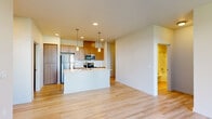 This single-floor residence showcases a clean, contemporary design highlighted by light hardwood flooring that flows through the main living areas. The open-concept kitchen serves as the focal point of the space, centered around a generous white-topped island with an undermount sink, ideal for both meal preparation and casual dining. Warm medium-toned wood cabinetry lines the walls, complemented by a white subway tile backsplash and a full suite of stainless steel appliances, including a refrigerator, range, and built-in microwave. Pendant lighting hangs above the island, adding a refined touch to the kitchen's overall aesthetic.

The living area extends naturally from the kitchen, offering an open and versatile layout. Bedrooms feature soft wall-to-wall carpeting, ceiling fans, and windows that allow natural light in, with each room offering access to a walk-in closet with built-in shelving. One bedroom includes a sliding door to an additional space.

The bathrooms maintain the unit's consistent design language, featuring wood-toned vanities with white countertops. The primary bathroom includes a double-sink vanity and a glass-enclosed walk-in shower, while a secondary bathroom offers a full soaking tub with shower combination.