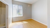 Unit 303 at 5043 Brooklyn Ave NE in Seattle's University District is a thoughtfully designed studio unit on the third floor. The open main living area features light bamboo hardwood flooring that reflects natural light streaming in through a large window fitted with vertical blinds, creating a bright and airy atmosphere. Neutral gray walls complement the clean, modern aesthetic throughout.

The compact kitchenette is efficiently arranged with rich dark-wood cabinetry extending to the ceiling for ample storage, a granite-style countertop, a built-in microwave, an electric cooktop, a single-basin sink, and a compact refrigerator — providing all essential cooking amenities in a space-conscious layout.

The bathroom is cleanly finished with a walk-in shower stall featuring white surround panels and a chrome showerhead, alongside a wall-mounted sink and a mirror. A separate toilet area is visible from the main living space through a white-framed doorway.

Additional features include a wall-mounted electrical panel, a baseboard heater, a fire alarm, and a solid wood entry door. The unit's efficient floor plan and natural light make it a functional and comfortable living space in the heart of Seattle.