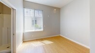 Unit 303 at 5043 Brooklyn Ave NE in Seattle's University District is a thoughtfully designed studio unit on the third floor. The open main living area features light bamboo hardwood flooring that reflects natural light streaming in through a large window fitted with vertical blinds, creating a bright and airy atmosphere. Neutral gray walls complement the clean, modern aesthetic throughout.

The compact kitchenette is efficiently arranged with rich dark-wood cabinetry extending to the ceiling for ample storage, a granite-style countertop, a built-in microwave, an electric cooktop, a single-basin sink, and a compact refrigerator — providing all essential cooking amenities in a space-conscious layout.

The bathroom is cleanly finished with a walk-in shower stall featuring white surround panels and a chrome showerhead, alongside a wall-mounted sink and a mirror. A separate toilet area is visible from the main living space through a white-framed doorway.

Additional features include a wall-mounted electrical panel, a baseboard heater, a fire alarm, and a solid wood entry door. The unit's efficient floor plan and natural light make it a functional and comfortable living space in the heart of Seattle.