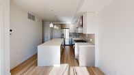 Located in the vibrant Marda Loop neighbourhood of Calgary, this thoughtfully designed one-bedroom, two-bathroom unit offers a contemporary and efficient living space. The open-concept kitchen is a standout feature, showcasing a large central island with a crisp white quartz countertop, flat-front cabinetry in soft neutral tones, a full suite of stainless steel appliances including a French door refrigerator, gas range, and dishwasher, complemented by a tasteful tile backsplash and pendant lighting overhead. Light-toned hardwood flooring runs throughout the main living areas, enhancing the bright and airy atmosphere. The bedroom is a calm, minimalist retreat with clean white walls and a generous picture window that frames expansive views of the Calgary cityscape and surrounding rooftops — an abundance of natural light filling the room throughout the day. The bathrooms are finished to a high standard, with one featuring large-format tile flooring, a floating vanity with ample storage, and a full glass-enclosed shower adorned with elegant marble-style tile from floor to ceiling. The overall design of the space is modern and refined, with a consistent neutral palette and quality finishes that create a cohesive, polished aesthetic throughout.