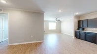 This single-story residence is designed with a clean, neutral aesthetic throughout, featuring light wood-look flooring that runs continuously across the living, bedroom, and kitchen areas. The open living space is generously proportioned, with crown molding accenting the ceiling and a ceiling fan providing both light and airflow. A window at the far end of the living area allows natural light to brighten the room, creating a welcoming atmosphere.

The kitchen is a standout feature, offering ample cabinetry in a rich dark espresso finish paired with light-toned countertops and a tile backsplash. Black appliances — including a refrigerator, range with overhead ventilation, and microwave — are included. Recessed lighting and crown molding complete the kitchen's polished look.

The bedrooms are well-sized with neutral walls, wood-look flooring, and windows fitted with blinds. Each bedroom includes a closet with built-in rod storage. The bathroom is thoughtfully designed with accessibility in mind, featuring grab bars, tile flooring, a vanity with dark cabinetry, and a separate water closet. Overall, the space offers a functional, modern layout with consistent finishes throughout.