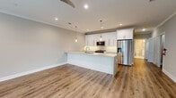 Located at 116 Starlight Walk in Holbrook, NY, this single-floor residence showcases a thoughtfully designed open-concept layout with contemporary finishes throughout. The kitchen serves as the centerpiece of the living space, featuring a large island with a striking marble-veined quartz countertop, an undermount sink, and elegant pendant lighting overhead. Crisp white shaker cabinetry extends to the ceiling, providing ample storage, while a full suite of stainless steel appliances—including a gas range, built-in microwave, dishwasher, and French door refrigerator—completes the space. The kitchen flows seamlessly into an open living area, unified by warm, wood-tone luxury vinyl plank flooring and neutral gray walls that lend a clean, modern aesthetic. Crown molding and recessed lighting are consistent throughout, adding refined detail. The bedroom offers natural light through a large window and features dual closets with built-in shelving and organizational systems. The bathroom is finished with floor-to-ceiling marble-style tile, a combination tub and shower with a glass sliding door, a white vanity with quartz countertop, and a classic basketweave tile floor, creating a polished, spa-like atmosphere.