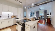 This single-floor residence showcases a thoughtfully designed open-concept layout that seamlessly connects the kitchen, dining, and living areas. The kitchen is a standout feature, outfitted with white shaker cabinetry, white quartz countertops, a classic subway tile backsplash, stainless steel appliances, and a central island with bar seating — ideal for both cooking and casual dining. Pendant lighting and track lighting illuminate the space, while exposed industrial ductwork adds an urban loft aesthetic to the soaring ceilings.

The living area flows naturally from the kitchen and is anchored by rich hardwood flooring, a ceiling fan, and floor-to-ceiling sliding glass doors that open to a private outdoor patio, bringing in generous natural light and outdoor views.

The bedroom offers a comfortable retreat with vaulted ceilings, a ceiling fan, natural light from well-positioned windows, hardwood floors, and direct access to the bathroom. Two bathrooms are present, each featuring white vanities with quartz countertops, tile flooring, and access to well-organized walk-in closets with built-in shelving. One bathroom includes a glass-enclosed shower, while the other features a shower-tub combination, offering versatility for different needs.