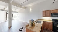 Located in the heart of Dayton, Ohio, Unit 206 at 35 S St. Clair St blends industrial character with modern comfort in a thoughtfully designed single-floor layout. The open-concept living and kitchen area immediately impresses with soaring ceilings, exposed structural beams, and prominent industrial ductwork that lend an authentic loft aesthetic. Large windows flood the living space with natural light, enhancing the airy, spacious feel of the main area. Durable hardwood-style flooring flows throughout, anchoring the design with warmth and continuity.

The kitchen features a peninsula countertop with granite-style surfaces, a double sink, and rich warm-toned cabinetry, providing both functionality and style. A structural column adds architectural interest to the open living area, further emphasizing the building's industrial heritage.

A long hallway connects the main living space to the private areas of the unit, with exposed ductwork running overhead, maintaining the loft-style character throughout. The bedroom is a cozy, well-proportioned retreat featuring a transom-style window that brings in soft, diffused light.

Both bathrooms are finished with dark wood vanities, white countertops, and hardwood-style flooring. Each features a shower and toilet, offering practical layouts with clean, neutral finishes. The unit presents a compelling blend of urban industrial design and everyday livability in a central Dayton location.