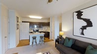 Located at 1431 W Nine Mile Rd in Pensacola, Florida, this single-floor unit offers a well-designed open-concept layout that seamlessly connects the kitchen and living areas. The kitchen is a standout feature, outfitted with dark espresso cabinetry, stainless steel appliances including a microwave, range, and dishwasher, and a light-toned countertop that provides ample prep space. A peninsula-style breakfast bar with bar stools creates an inviting spot for casual dining or entertaining. The living area is carpeted and finished in soft, neutral tones, creating a warm and relaxed ambiance. Large white walls offer a bright, clean backdrop throughout the space, while recessed and flush-mounted lighting ensures the interior is well-lit. Smooth transitions between the hard flooring of the kitchen and the carpeted living space add to the cohesive flow of the layout. Crown molding accents the ceilings, adding a subtle architectural detail that elevates the overall finish of the unit. The open floor plan allows natural sightlines across the entire main living space, making the unit feel airy and connected. This residence combines functional design with comfortable living in a conveniently located Pensacola address.