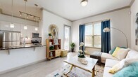 This thoughtfully designed one-bedroom, one-bathroom residence offers a functional and stylish single-floor layout. Light wood-tone flooring runs throughout, creating a cohesive and airy feel across all rooms.

The living room serves as the heart of the home, featuring large windows dressed with elegant navy drapes that invite an abundance of natural light. Crown molding along the ceiling adds a refined architectural touch, while a sliding door provides access to the outdoors.

The galley-style kitchen is efficiently laid out with white cabinetry, dark granite countertops, a tiled backsplash, and stainless steel appliances including a refrigerator, range, microwave, and dishwasher. A window above the counter adds natural light to the workspace.

The bedroom is a serene retreat, offering generous proportions, large windows with blinds, crown molding, and ample space for a full bedroom suite. A dedicated closet provides practical storage.

The bathroom features white cabinetry with a dark granite vanity top, a large mirror with overhead lighting, and a combined shower and tub area. The space is clean and well-appointed with a neutral color palette throughout.

Overall, this residence combines modern finishes with practical design, creating a comfortable and inviting living environment.