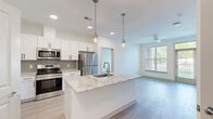 Located in Chester, VA, this thoughtfully designed 2-bedroom, 2-bathroom residence offers a clean, modern aesthetic across a single-level, open-concept floor plan. The kitchen serves as a central highlight, showcasing a large granite-topped island with an undermount sink and stylish pendant lighting, white shaker cabinetry with matte black hardware, a gray tile backsplash, and a full suite of stainless steel appliances. Light wood-tone flooring runs throughout, lending a cohesive and contemporary feel to every room. The living area benefits from large windows and a ceiling fan, allowing abundant natural light and outdoor views of the surrounding greenery. The spacious primary bedroom includes its own en-suite bathroom featuring granite countertops, white cabinetry, and direct access to a dedicated walk-in closet. The second bathroom offers a clean, white-tiled tub-shower combination with brushed nickel fixtures. The second bedroom is well-proportioned, with a window framing outdoor views and neutral finishes that make it versatile for various uses. Two closets provide ample storage throughout the residence. The overall design palette — white walls, light flooring, and modern fixtures — creates a bright, move-in-ready environment with a polished, upscale character.