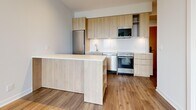 Located at 25 Nicholas in Toronto's vibrant St. James Town neighbourhood, this one-bedroom, one-bathroom unit offers a thoughtfully designed layout with a clean, modern aesthetic. Light hardwood flooring runs throughout the space, creating a warm and cohesive feel.

The kitchen is a standout feature, showcasing natural wood cabinetry that extends to the upper wall, a crisp white backsplash, and a full suite of stainless steel appliances including a refrigerator, stove, dishwasher, and built-in microwave. A peninsula island provides additional counter space and open shelving, making the kitchen both functional and visually appealing.

The bedroom is a bright, comfortable retreat with large floor-to-ceiling windows that frame views of the surrounding Toronto cityscape and greenery, allowing ample natural light to fill the room. A mirrored closet adds practicality while enhancing the sense of space.

The bathroom is finished in a clean, contemporary style with large-format beige floor tiles, white subway wall tiles, a soaking tub with overhead rain shower, and a wood-fronted vanity with a white countertop and integrated sink.

The unit's neutral palette, warm wood tones, and modern finishes create a cohesive and inviting atmosphere throughout.