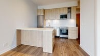Located at 25 Nicholas in Toronto's vibrant St. James Town neighbourhood, this one-bedroom, one-bathroom unit offers a thoughtfully designed layout with a clean, modern aesthetic. Light hardwood flooring runs throughout the space, creating a warm and cohesive feel.

The kitchen is a standout feature, showcasing natural wood cabinetry that extends to the upper wall, a crisp white backsplash, and a full suite of stainless steel appliances including a refrigerator, stove, dishwasher, and built-in microwave. A peninsula island provides additional counter space and open shelving, making the kitchen both functional and visually appealing.

The bedroom is a bright, comfortable retreat with large floor-to-ceiling windows that frame views of the surrounding Toronto cityscape and greenery, allowing ample natural light to fill the room. A mirrored closet adds practicality while enhancing the sense of space.

The bathroom is finished in a clean, contemporary style with large-format beige floor tiles, white subway wall tiles, a soaking tub with overhead rain shower, and a wood-fronted vanity with a white countertop and integrated sink.

The unit's neutral palette, warm wood tones, and modern finishes create a cohesive and inviting atmosphere throughout.