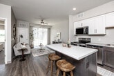 Located in Clear Lake, Iowa, this thoughtfully designed 2-bedroom, 1-bathroom residence offers a clean, contemporary aesthetic across a single floor. The open-concept layout connects the kitchen and living room seamlessly, maximizing the efficient use of space. The kitchen is a standout feature, showcasing white upper cabinetry paired with dark lower cabinets, a full suite of stainless steel appliances, and a central island with a light quartz countertop and bar seating — ideal for both cooking and casual dining. Durable wood-look flooring runs throughout the main living areas, complementing the neutral color palette. The living room is bright and inviting, featuring a ceiling fan, large sliding glass door with vertical blinds that floods the space with natural light and provides outdoor views. Both bedrooms are carpeted and finished with soft, neutral tones; the primary bedroom features a generously sized window with pleasant outdoor views. The full bathroom includes a tub/shower combination, a dark-cabineted vanity with a white countertop, and wood-look flooring. A dedicated laundry room with full-size washer and dryer and wire shelving overhead adds everyday convenience to this well-appointed home.