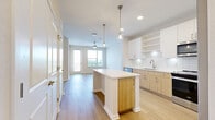 Located in Longwood, Florida, this well-appointed one-bedroom, one-bathroom unit offers a thoughtfully designed open-concept layout. The combined living, dining, and kitchen area forms the heart of the home, featuring light wood-tone luxury vinyl plank flooring, recessed lighting, and a ceiling fan. The modern kitchen is equipped with stainless steel appliances, a center island with white quartz countertops, two-tone cabinetry in white and natural wood, a classic subway tile backsplash, and stylish pendant lighting. A private balcony accessible from the living area offers expansive views of lush greenery and the surrounding Longwood landscape under open Florida skies. The generously sized bedroom features plush carpeting, a ceiling fan, and a large window that brings in abundant natural light. The full bathroom includes a soaking tub with white subway tile surround and gold-tone fixtures, complemented by natural wood vanity cabinetry and a clean white quartz countertop. Three closets provide ample storage, including a spacious walk-in closet with wire shelving. A dedicated in-unit laundry area adds everyday convenience. The unit presents a cohesive, contemporary aesthetic with a neutral color palette throughout.