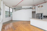 Located at 1080 Euclid Ave NE in Atlanta's dynamic Little Five Points neighborhood, this single-floor loft showcases a striking industrial aesthetic throughout. The open-plan living area is defined by warm hardwood floors, soaring ceilings, and exposed galvanized ductwork with distinctive red fire suppression piping overhead — hallmark features of a converted industrial building. Large, multi-pane grid windows line the walls, flooding the space with abundant natural light and offering lush, tree-lined views of the surrounding neighborhood.

The kitchen is thoughtfully designed with white shaker-style cabinetry, granite countertops, and a central peninsula that provides additional prep and seating space. Stainless steel appliances, including a full-size refrigerator and built-in microwave, complement the sleek dark tile backsplash. Industrial-style pendant lighting over the peninsula ties the kitchen seamlessly to the loft's overall design character.

The bathroom continues the refined aesthetic with granite countertops on a white vanity cabinet, an undermount sink, a large wall mirror with modern lighting, and wood-look flooring that echoes the warmth found throughout the rest of the unit. Brushed nickel fixtures and grab bars add both style and practicality. Together, these elements create a cohesive, urban loft environment full of character and charm.