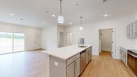 Located at 15 Ore Bank Rd in Dillsburg, PA, this thoughtfully designed one-bedroom, one-bathroom unit offers a clean, modern aesthetic across a single well-organized floor. The open-concept kitchen and living area forms the heart of the space, anchored by a large center island with a white quartz countertop, undermount sink, and built-in dishwasher. Gray shaker-style cabinetry lines the kitchen walls, complemented by a full suite of stainless steel appliances including a refrigerator, range, and microwave. Pendant lighting above the island adds a contemporary touch, while recessed lighting illuminates the entire open area. Light-toned hardwood flooring flows throughout the main living spaces, creating a warm and cohesive feel. The living area is spacious and bright, with sliding glass doors that open to an outdoor view, inviting natural light deep into the room. The bedroom features plush carpeting and a window with exterior views, offering a comfortable and quiet retreat. An additional bonus room with carpet provides flexible space for a home office or storage. The full bathroom is finished with gray cabinetry, a white vanity top, and a tub-shower combination. A utility room completes the layout, adding practical functionality to this well-appointed unit.